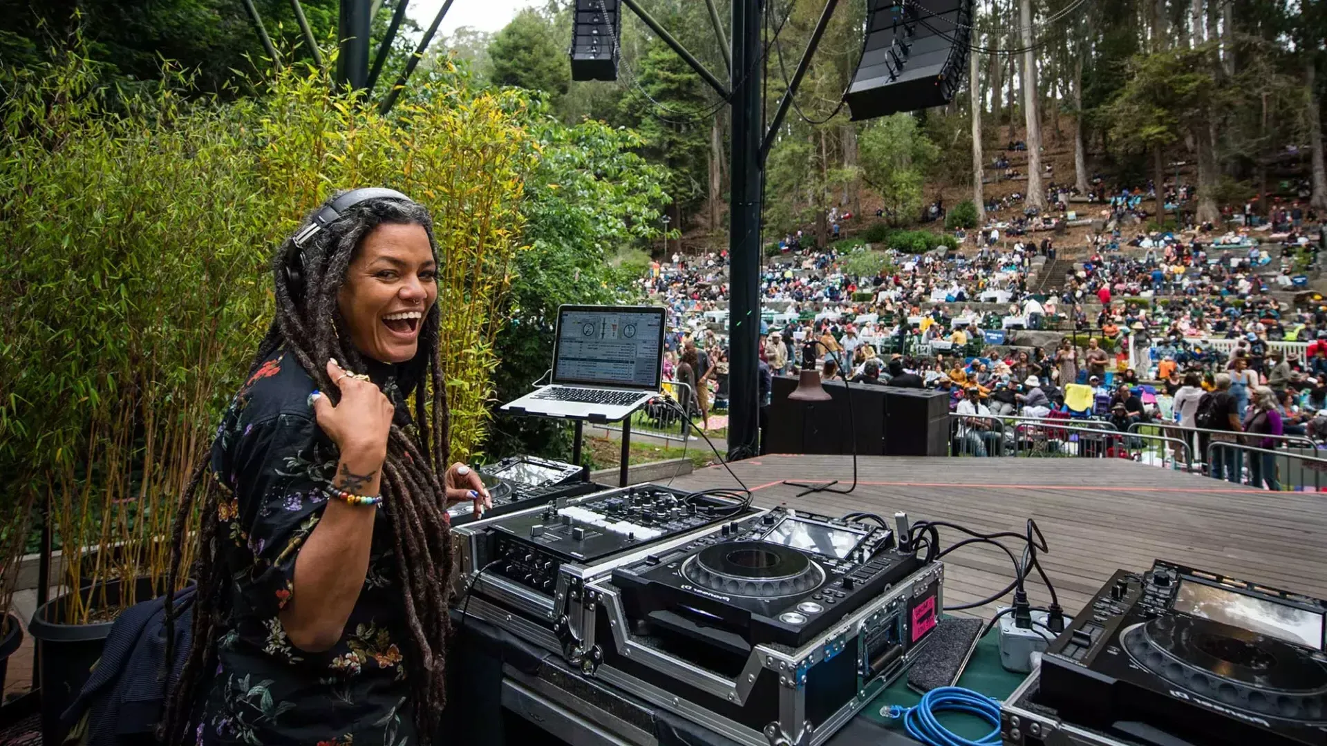 A woman DJing at the Stern Grove Festival looks over her shoulder and smiles into the camera.